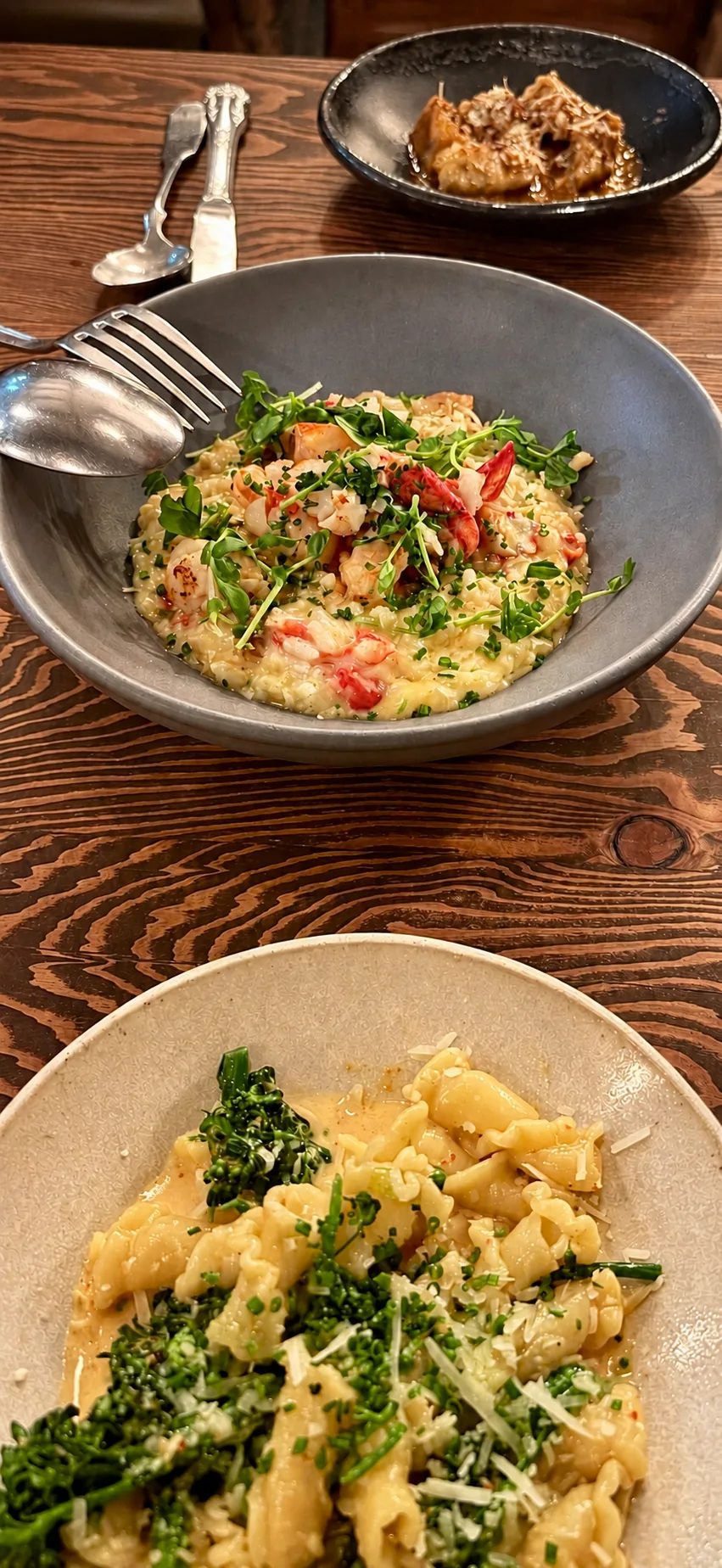 Risotto and pasta in ceramic dishes on a wooden dining table.